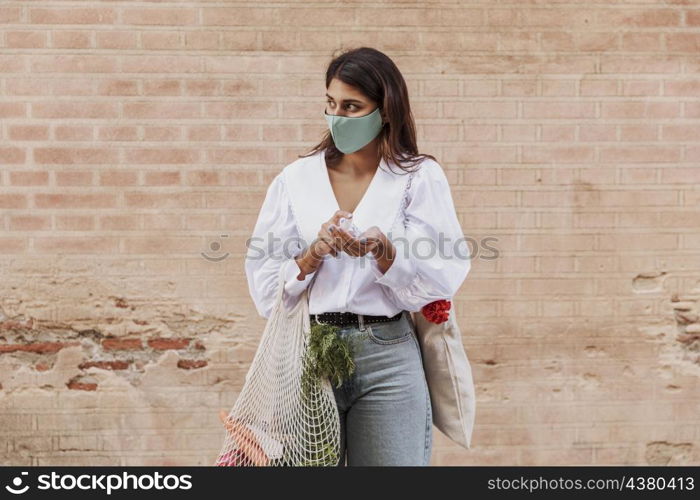 woman with face mask grocery bags using hand sanitizer