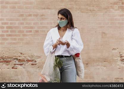 woman with face mask grocery bags using hand sanitizer