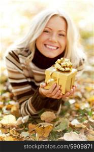 Woman with gift laying on dry autumn leaves. Woman with gift