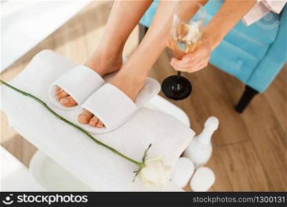Woman with glass of champagne near the foot bath, beauty salon. Professional beautician service, female customer, skin and body care in spa studio