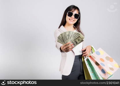 Woman with glasses confident shopper smile holding online shopping bags multicolor and dollar money banknotes on hand, excited happy Asian young female person studio shot isolated on white background