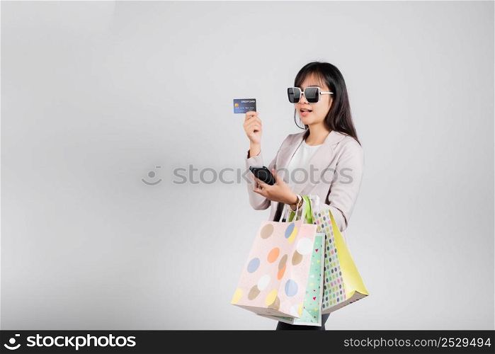 Woman with glasses shopper smile hold online shopping bags, smartphone and credit card for payment, Portrait excited happy Asian female sale mobile financial application isolated on white background