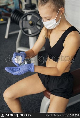 woman with gloves medical mask gym using hand sanitizer
