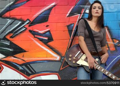 Woman with guitar in front of graffiti