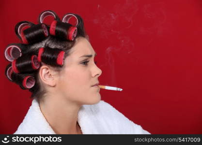 woman with hair curlers against red background smoking