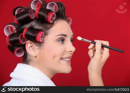 Woman with hair curlers applying make-up