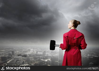 Woman with hammer. Rear view of woman in red coat with hammer in hands