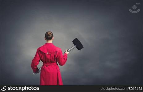 Woman with hammer. Rear view of woman in red coat with hammer in hands