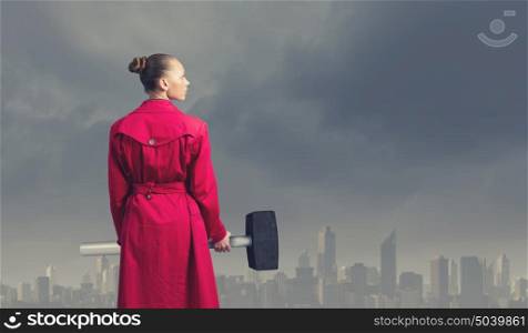 Woman with hammer. Rear view of woman in red coat with hammer in hands