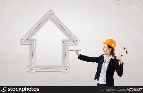 Woman with hammer. Young businesswoman hitting nail in house model with hammer
