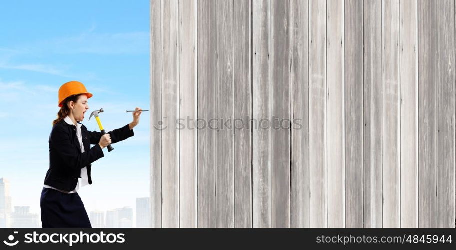 Woman with hammer. Young businesswoman hitting nail in wall with hammer