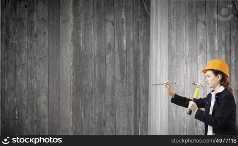 Woman with hammer. Young businesswoman hitting nail in wall with hammer