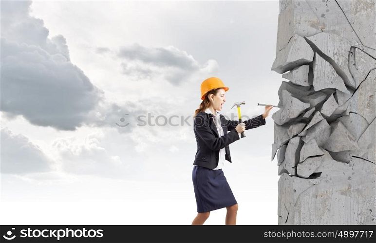 Woman with hammer. Young businesswoman hitting nail in wall with hammer