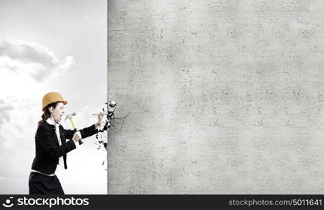 Woman with hammer. Young businesswoman hitting nail in wall with hammer