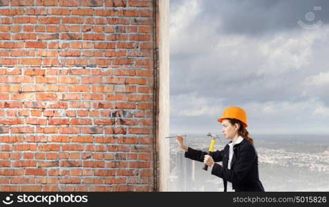 Woman with hammer. Young businesswoman hitting nail in wall with hammer