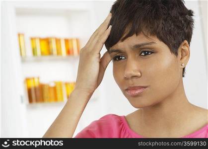 Woman with hand on head, near pill cabinet