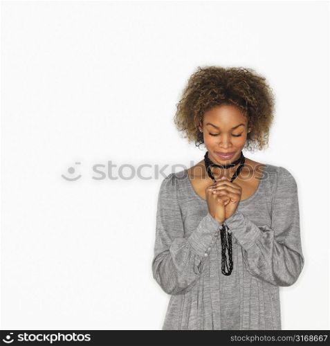 Woman with hands clasped together in prayer and eyes closed.