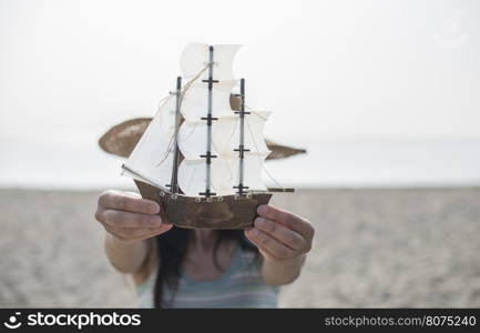 Woman with hat hold boat model on the beach