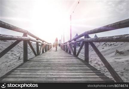Woman with hat on wooden trail on the beach in the morning. Sunrise