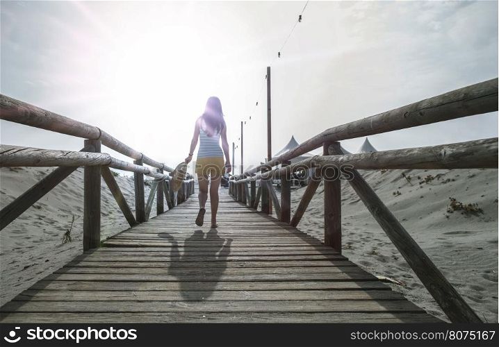 Woman with hat on wooden trail on the beach in the morning. Sunrise