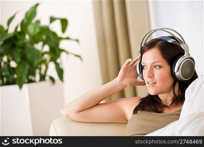 Woman with headphones listen to music in lounge, plant in background