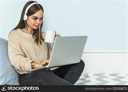 woman with headphones using laptop having coffee home during pandemic