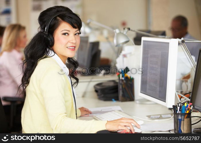 Woman With Headset Working At Desk In Busy Creative Office