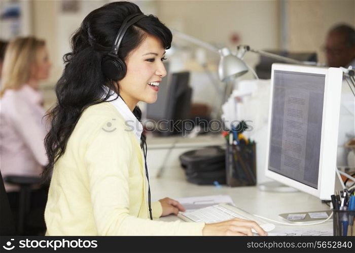 Woman With Headset Working At Desk In Busy Creative Office
