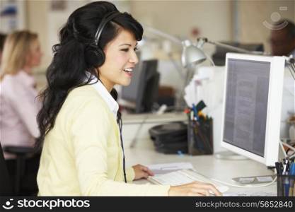 Woman With Headset Working At Desk In Busy Creative Office