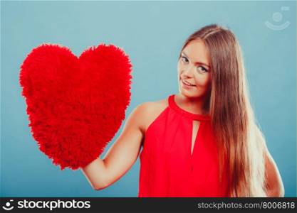 Woman with heart shape pillow. Valentines day love. Smiling pretty cute young woman girl with red heart shape pillow in studio on blue. Valentines day love.