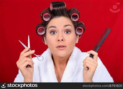 Woman with her hair in curlers holding scissors and a comb