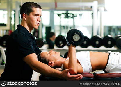 Woman with her personal fitness trainer in the gym exercising with dumbbells