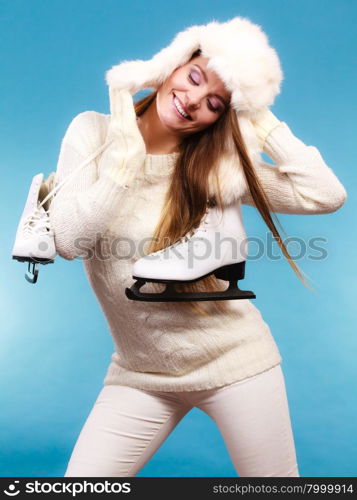 Woman with ice skates getting ready for ice skating . Woman with ice skates getting ready for ice skating. Winter sport activity. Smiling girl wearing warm clothing sweater and fur cap on blue studio shot