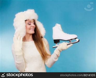 Woman with ice skates getting ready for ice skating . Woman with ice skates getting ready for ice skating. Winter sport activity. Smiling girl wearing warm clothing sweater and fur cap on blue studio shot