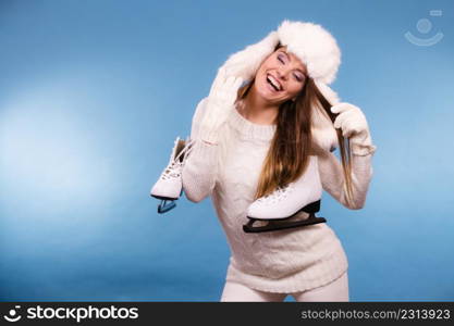 Woman with ice skates getting ready for ice skating. Winter sport activity. Smiling girl wearing warm clothing sweater and fur cap on blue studio shot. Woman with ice skates getting ready for ice skating.