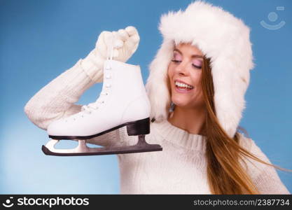 Woman with ice skates getting ready for ice skating. Winter sport activity. Smiling girl wearing warm clothing sweater and fur cap on blue studio shot. Woman with ice skates getting ready for ice skating.