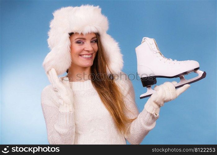 Woman with ice skates getting ready for ice skating. Winter sport activity. Smiling girl wearing warm clothing sweater and fur cap on blue studio shot. Woman with ice skates getting ready for ice skating.