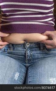 Woman with jeans shows her belly. Overweight.