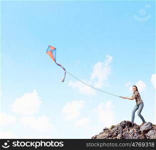 Woman with kite. Young pretty woman standing on rock with colorful kite