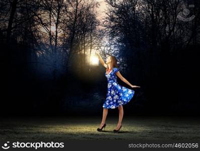Woman with lantern. Young woman in blue dress walking in night wood