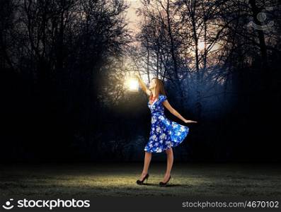 Woman with lantern. Young woman in blue dress walking in night wood