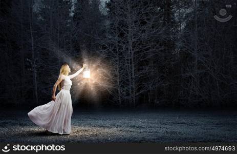 Woman with lantern. Young woman in white long dress walking in night wood