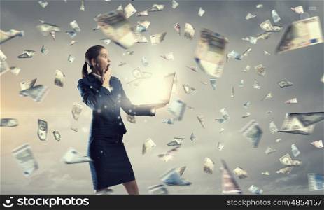 Woman with laptop in hands. Attractive shocked businesswoman with laptop in hands and money falling from sky