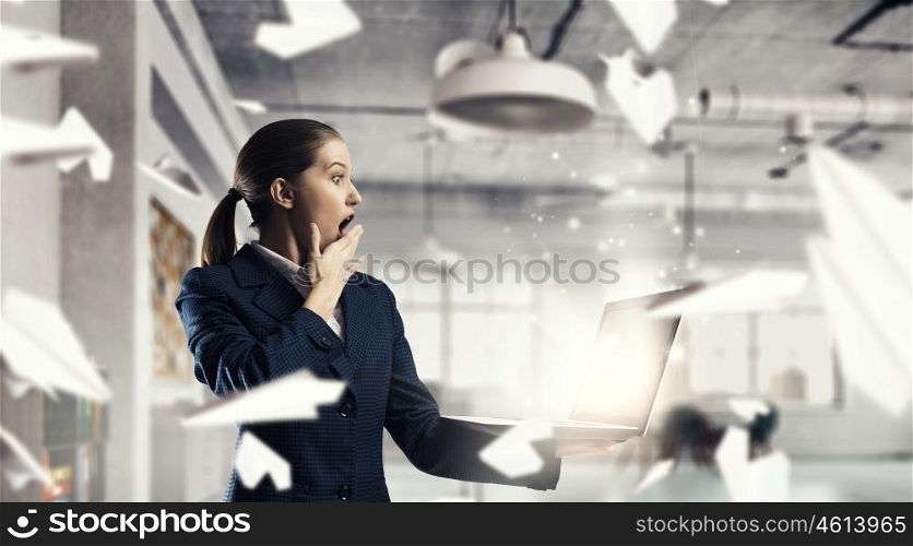 Woman with laptop in hands mixed media. Attractive shocked businesswoman with laptop in hands in modern office interior