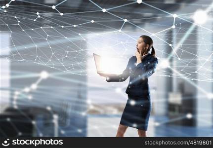 Woman with laptop in hands mixed media. Attractive shocked businesswoman with laptop in hands in modern office interior