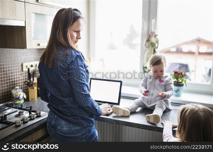 woman with laptop looking her children kitchen