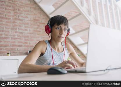 Woman with laptop working at home while listening music by headphones. Marta Rodriguez.jpg