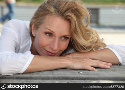 Woman with long blonde hair leaning on a bench