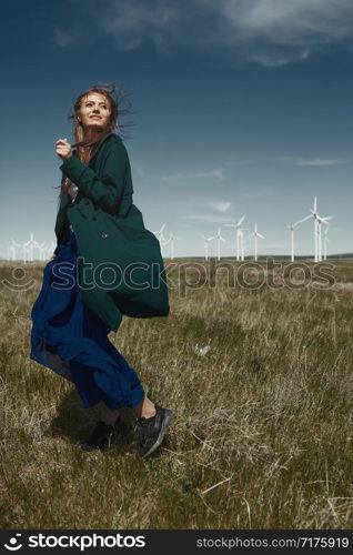 Woman with long tousled hair next to the wind turbine with the wind blowing