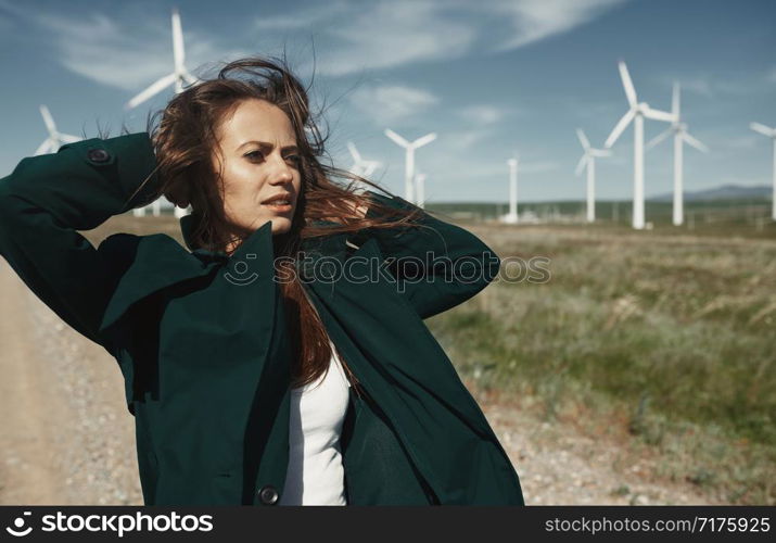 Woman with long tousled hair next to the wind turbine with the wind blowing